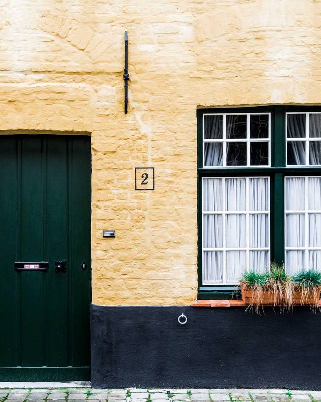A pale stone facade with a green door and a window with plants.