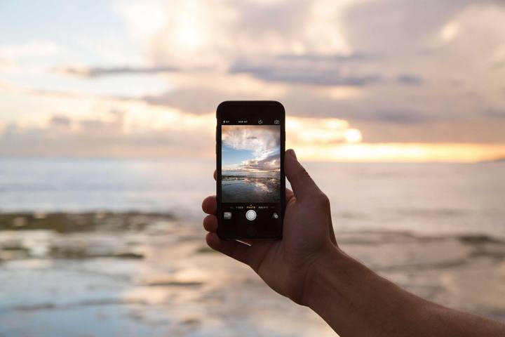 A hand filming vertically with a phone in front of the sea at sunset.