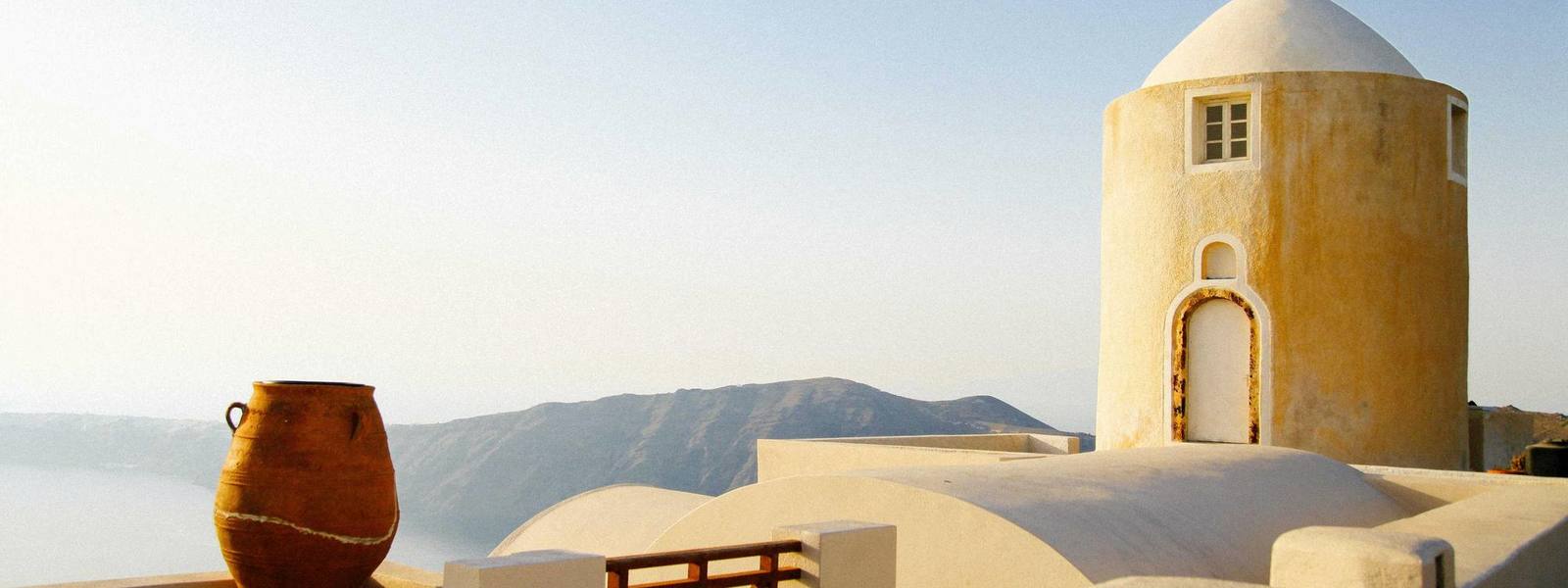 A whitewashed Mediterranean terrace with a clay jar and the sea behind.